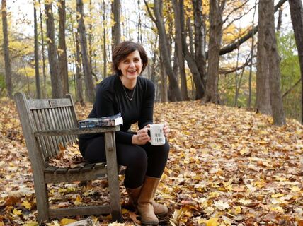 Jill Hinton sitting on bench in woods drinking coffee